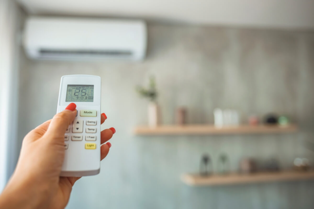 Hand with remote control directed on air conditioner.