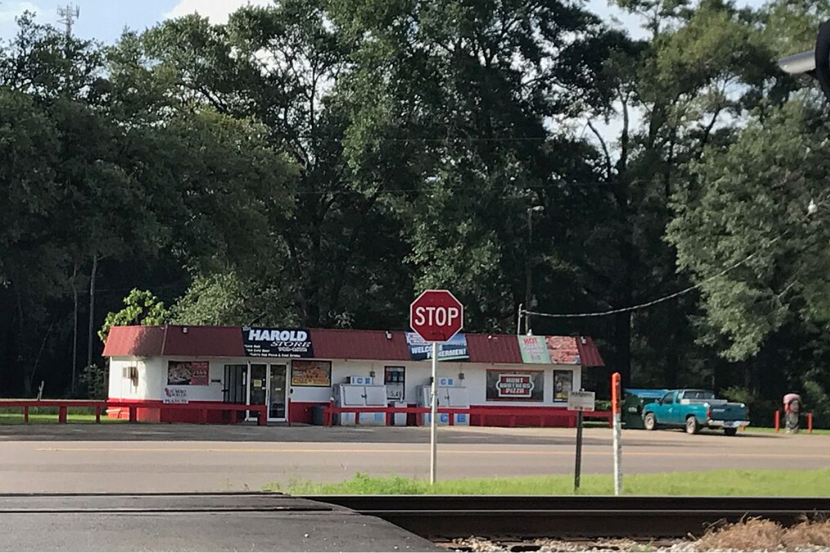 A red stop sign stands on the side of a road in front of Harold Store
