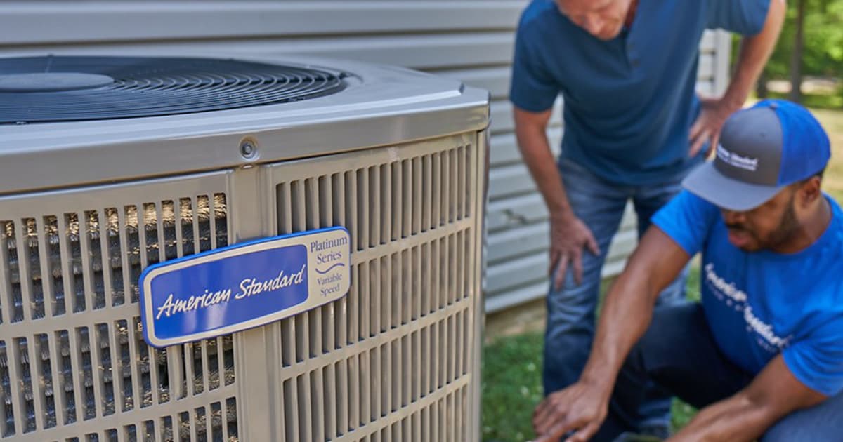 A professional HVAC technician from McNorton discusses a repair with a homeowner next to an American Standard air conditioning unit.
