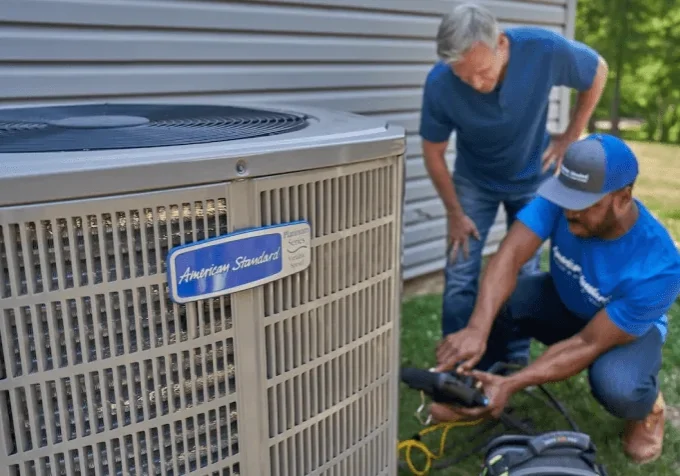 A McNorton HVAC technician in uniform shows a homeowner the repair work needed on their American Standard Platinum Series air conditioner.
